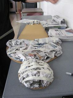 a table topped with lots of newspapers and paper wrapped in tape next to a pair of shoes