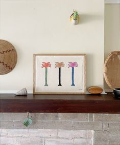 a fire place with some art on top of it and two baskets hanging from the wall