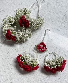 three pieces of red and white flowers are arranged on a counter top with earrings, necklace and earring