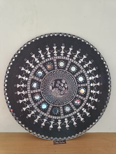 a black plate with designs on it sitting on top of a wooden table next to a white wall