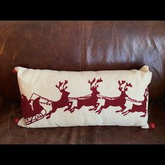 a red and white pillow with santa's sleigh on it sitting on a brown leather couch