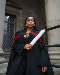 a woman dressed in black and red holding a large white object on her shoulder while standing next to some stairs