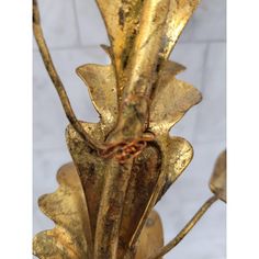 a gold colored metal vase with flowers and leaves on the top, in front of a white brick wall