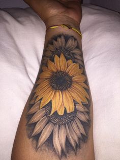 a sunflower tattoo on the arm of a person laying in bed with white sheets