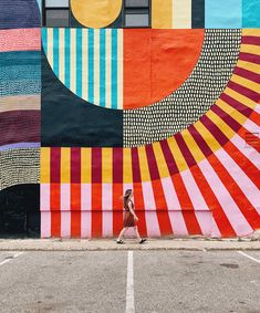 a woman walking past a colorful wall on the side of a building