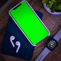 an apple watch and green screen sitting next to each other on a wooden table with ear buds