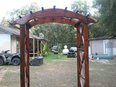 a wooden arch in the middle of a yard next to a house and car parked on the other side