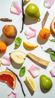 various fruits are arranged on a white surface with pink flowers and green leafy leaves