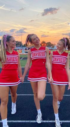 three girls in cheerleader outfits walking on a track