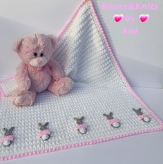 a pink teddy bear sitting on top of a crocheted blanket with pins attached to it