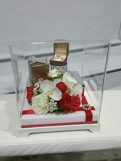 a glass display case with flowers and rings on it's sides, sitting on a white surface