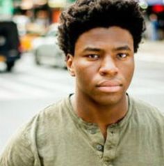 a young man standing on the street with his hands in his pockets and looking at the camera