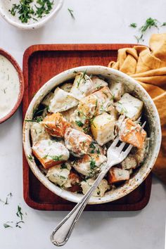 a bowl of potato salad with a fork in it and some bread on the side