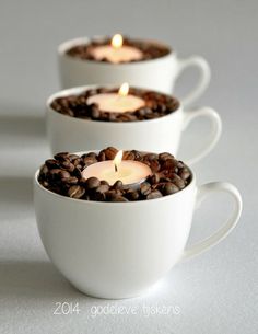 three cups filled with coffee beans and lit candles