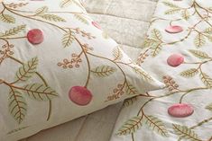 a close up of a pillow on a bed with pink flowers and leaves embroidered on it