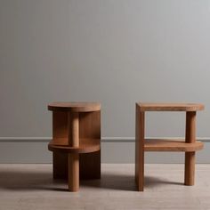 two wooden tables sitting next to each other on top of a tile floor in front of a gray wall