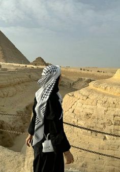 a man standing in front of the pyramids with his head covered by a scarf