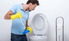 a man in blue shirt and yellow gloves holding a plunger next to a toilet