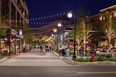 people are walking down the street in front of shops and restaurants at night with lights strung over them