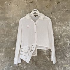 a white shirt hanging up against a wall with lace on the bottom and an open collar