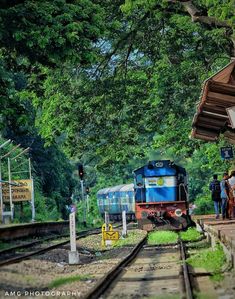 there is a blue train that is coming down the tracks and people are standing near it