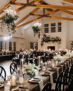 a banquet hall with tables and chairs set up for an event or function, surrounded by candles and greenery