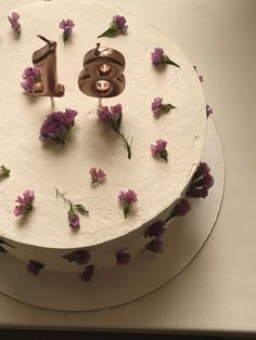 a white cake with purple flowers and a number one on the top is decorated in gold