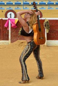 a woman with an acoustic guitar in front of a bull ring at a rodeo or competition