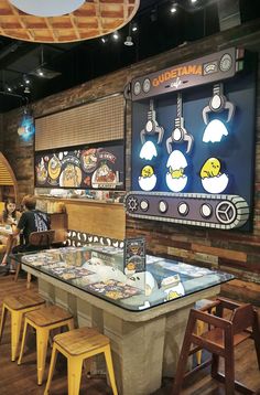 the inside of a restaurant with tables and stools in front of a large screen