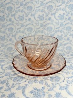 a glass cup and saucer sitting on top of a blue tablecloth covered table