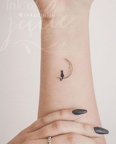 a woman's wrist with a cat on the moon tattoo