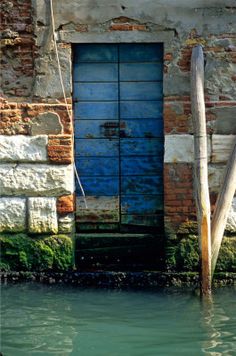 an old building with a blue door in the water next to a wooden pole that is sticking out of it's side