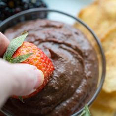 a person dipping a strawberry into a chocolate dip