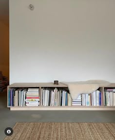 a bookshelf filled with lots of books next to a white wall and rug