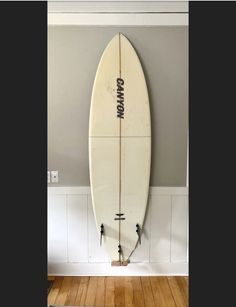 a white surfboard hanging on the wall in a room with wood floors and gray walls