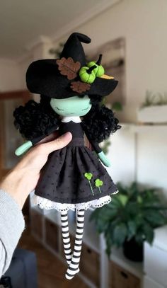 a person holding up a doll wearing a witches hat and black dress with green leaves on it