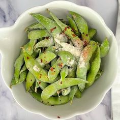 a white bowl filled with green beans covered in seasoning on top of a marble table