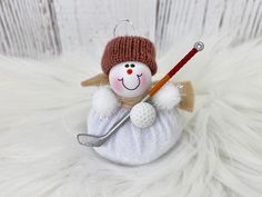 a snowman ornament with a golf club in it's hand on a white fur background