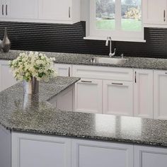 a kitchen with granite counter tops and white cabinets in the center, along with a vase filled with flowers