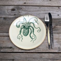 a plate with an octopus drawn on it next to a fork and knife sitting on a wooden table