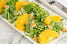 a white plate topped with orange slices and green salad next to silverware on a marble table