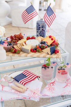 a table topped with cheese and fruit covered in american flag decorations on top of a glass table