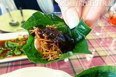 a person holding up some food on top of a green leafy dish at a table