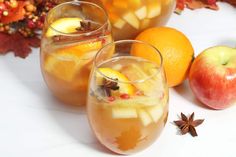 two glasses filled with apple cider next to oranges and star anise