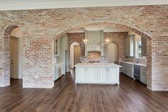 an empty kitchen and living room with brick walls, hardwood floors, and white cabinets