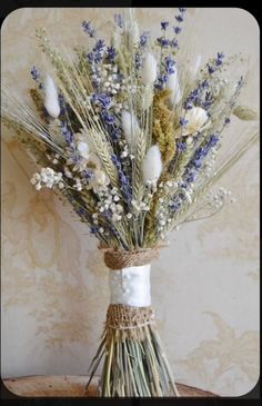 a bouquet of dried flowers in a vase on a table with a wallpapered background