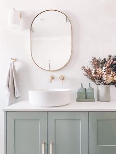 a bathroom with a round mirror above the sink and grey cupboards on either side