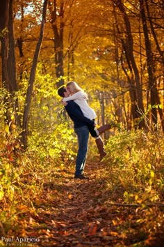 a man carrying a woman on his back while walking through the woods in fall colors