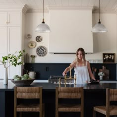 a woman standing at the kitchen counter in front of an island with four stools