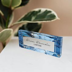 a blue and white glass name plate sitting on top of a table next to a potted plant